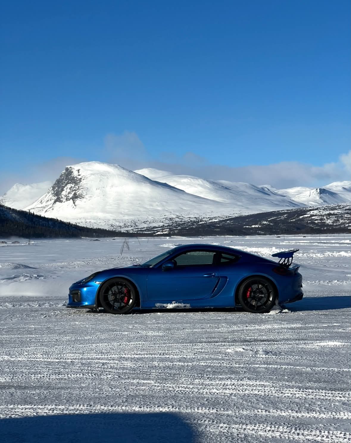 Blå Porsche sportsbil i profil på et snødekt fjell